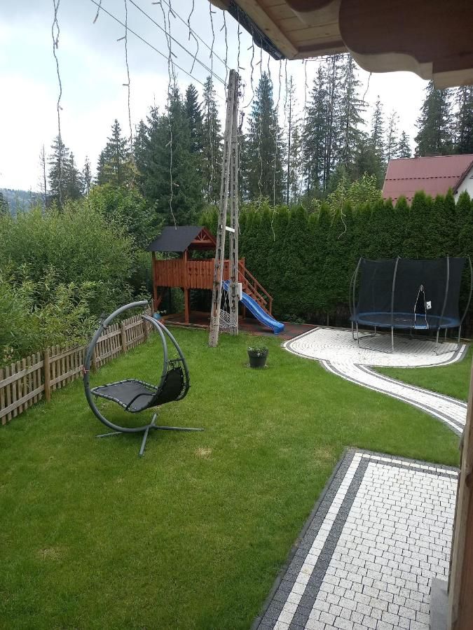 Ogród z trawnikiem, wiszącym fotelem i trampoliną