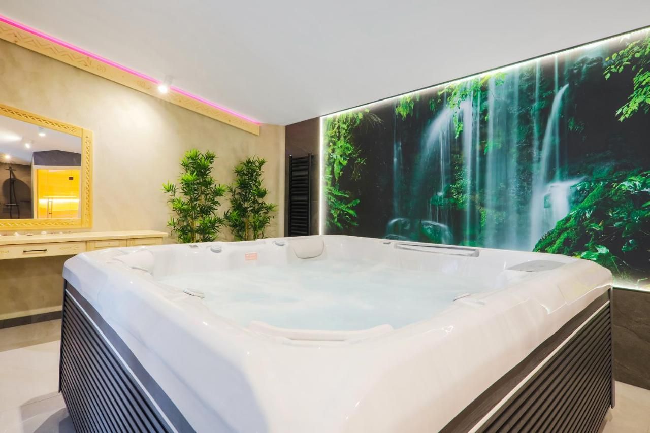Jacuzzi przed podświetloną ścianą z wodospadem i zielenią