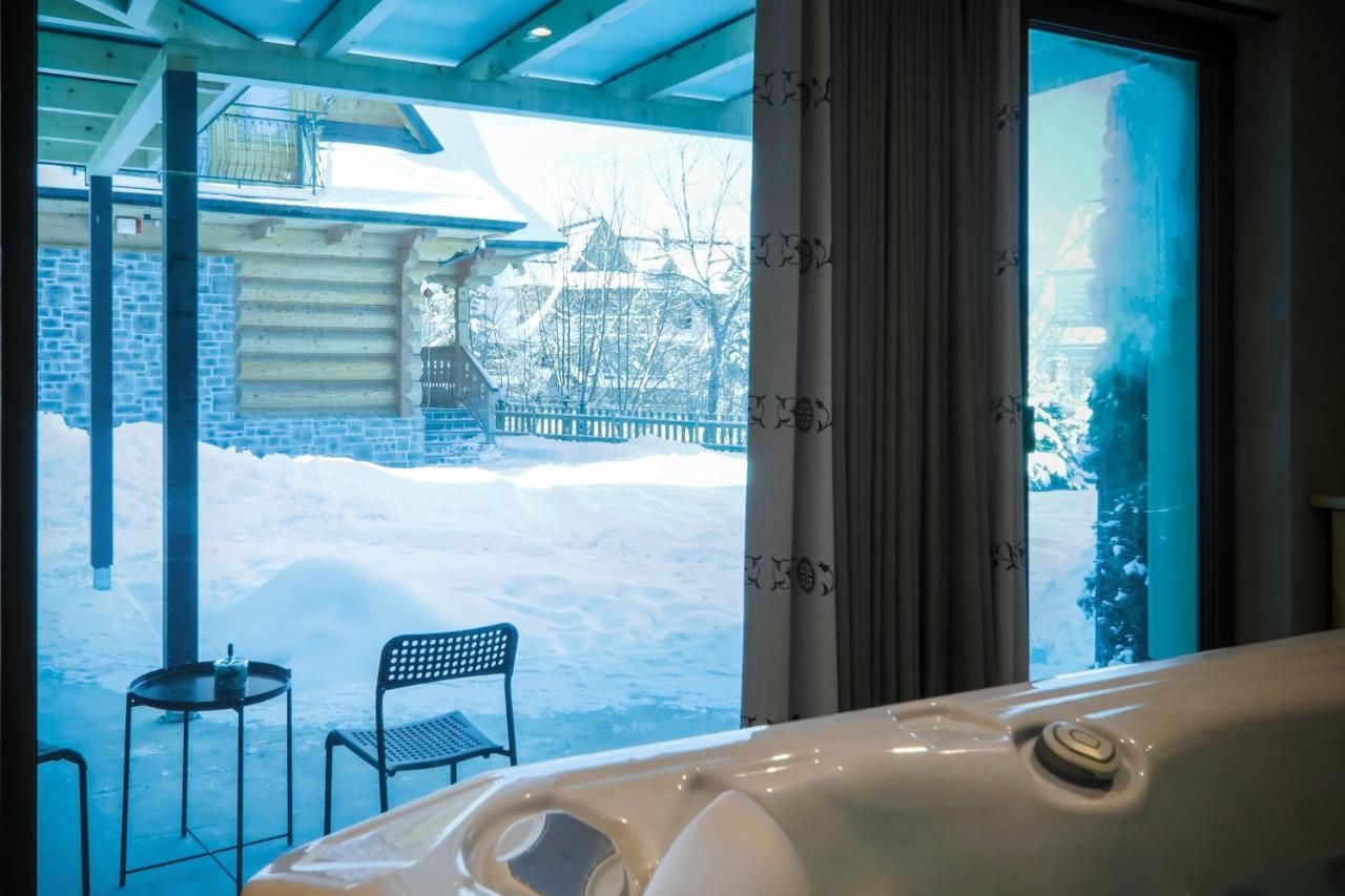 Widok z jacuzzi przez przeszklone drzwi na zaśnieżony ogród i dom