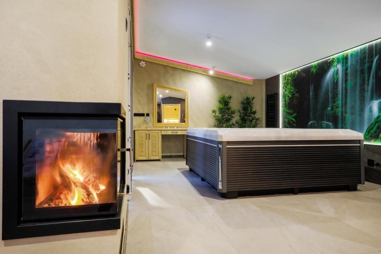 Ogień w kominku, w tle jacuzzi i ściana z wodospadem